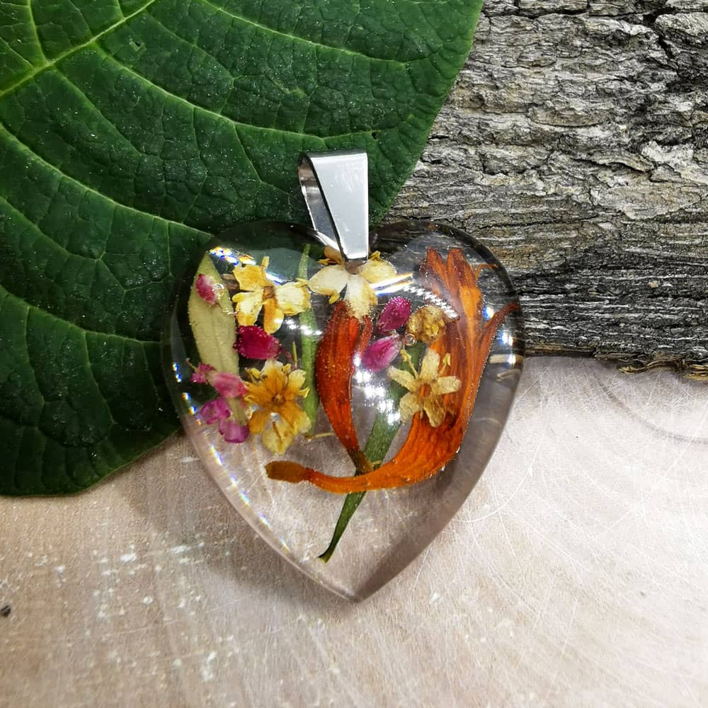 Ozdobny wisiorek w kształcie serca z płatkami kwiatów zatopionymi w przeźroczystej żywicy epoksydowej.