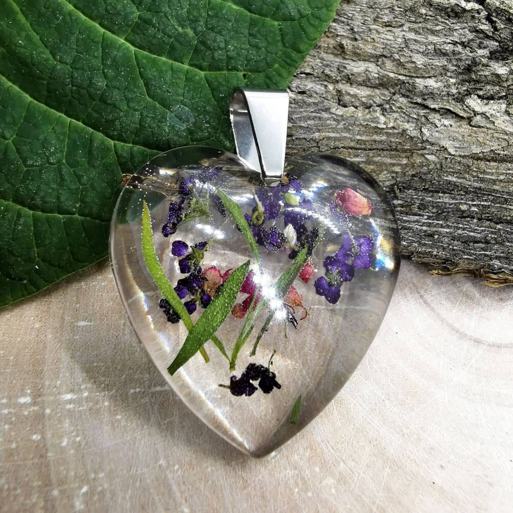 Ozdobny wisiorek w kształcie serca z płatkami kwiatów zatopionymi w przeźroczystej żywicy epoksydowej.